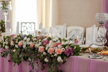 Head table with pink linen white chairs, and beautiful pink, white, and purple flowers