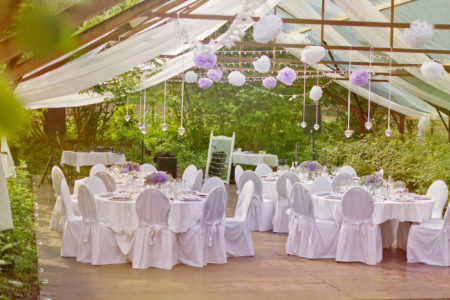 Romantic outdoor wedding in the old greenhouse- white tablecloth, empty glasses, white table setting, wild fresh flowers
