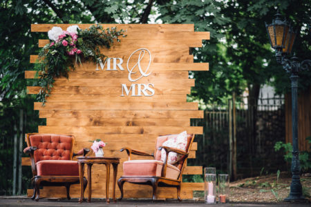 Wedding. Banquet. Mr. and Mrs. signs on wooden board decorated by flowers and greenery and lounge zone including chairs and tables.