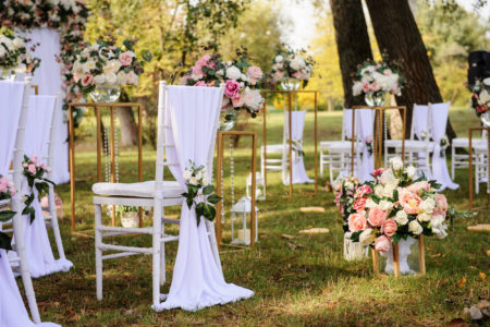 Preparation for a wedding ceremony outdoor in the park/ forest . Wood arch and chairs are decorated with white and pink flowers roses and peony, on the ground are many wood lanterns with candles.