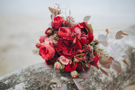 Wedding bouquet . The bride's bouquet. Bouquet of red and pink flowers, black berries and greenery, with a ribbon of color Marsala lies on a log by the lake