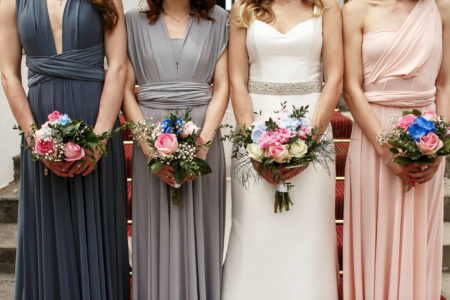 Bride and bridesmaids in pastel dresses stand in a ray with wedding bouquets