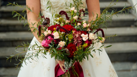 A bride holding a large wedding bouquet of red flowers.