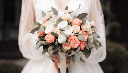 a girl in a white dress holds a wedding bouquet in her hands close-up