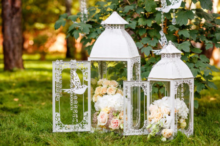 Wedding decor in rustic style.Two white vintage lamp with flowers inside standing on green grass
