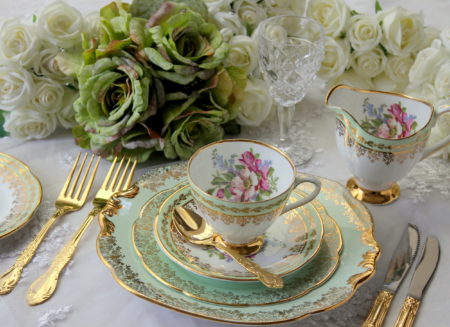 Vintage green teacup, saucer and plate with gold cutlery flatware and roses on a lace table cloth - wedding tea party