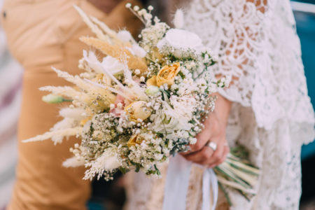 Wedding bouquet close up. Newlyweds in boho style are embracing, the bride is holding flowers in her hands.