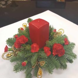 Holiday centerpiece of red flowers, red candle and winter greenery