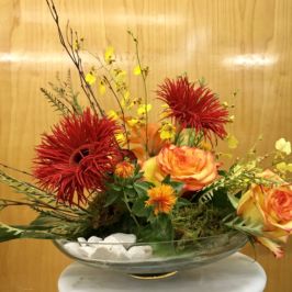 Low bowl flower arrangement of red and orange flowers
